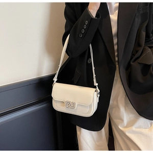 Creamy white leather crossbody bag with silver buckle worn by a model in a studio setting