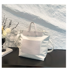 Detail of white tote bag featuring skull embossed pattern and faux crocodile texture trim