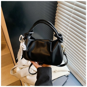 Detalle de bolso tipo cubo negro plisado con colgante de perlas y encaje y asa redonda