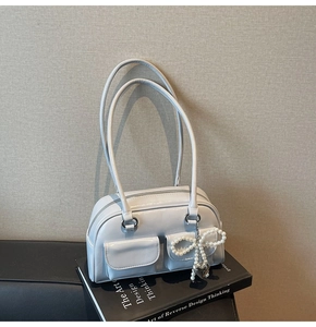 Detail of light blue faux leather handbag with pearl bow charm and twin front pockets