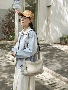 Detailed view of beige nylon dumpling bag with adjustable strap in outdoor setting
