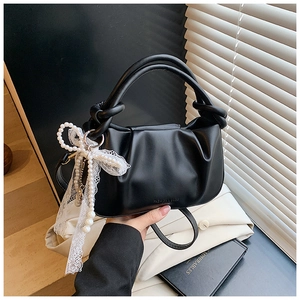 Detalle del bolso tipo cubo negro plisado con asa de nudo y colgante de encaje y perla