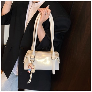 Close-up of cream glossy shoulder bag with charms and elegant silver hardware detail
