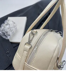 Detailed macro view of the cream leather texture and silver zipper hardware on a small bag