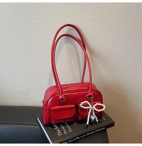 Detail of red glossy underarm bag featuring pearl bow charm and double front pockets