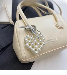 Detail of cream leather barrel bag featuring a heart-shaped pearl charm and lettering