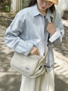 Detailed view of cream nylon dumpling bag with brand woven label shown in outdoor setting