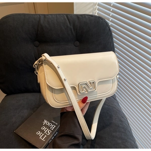 Close-up of cream white flap crossbody bag with geometric silver metal buckle on velvet