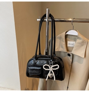 Detail of glossy black shoulder bag featuring a pearl bow charm and metal heart pendant
