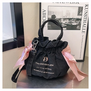 Détail du sac seau en denim noir avec nœuds en satin rose et logo D doré
