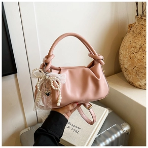 Detalle de bolso tipo cubo plisado rosa con lazo de perlas y colgante de corazón