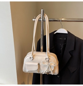 Detail of cream white shoulder bag featuring double front pockets and pearl bow charm