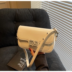 Detail of cream leather crossbody bag featuring silver N buckle and adjustable strap