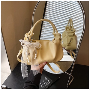 Detalle de bolso tipo cubo plisado amarillo con lazo de encaje y perlas elegantes