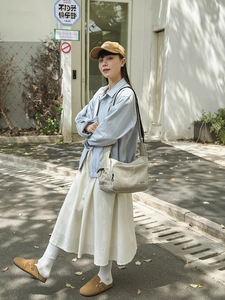 Outdoor lifestyle shot of a beige large nylon crossbody bag styled with a blue casual outfit