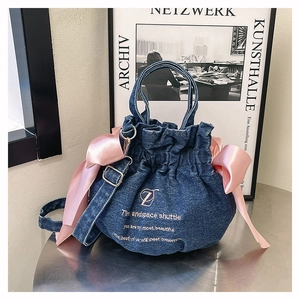Détail du sac seau en denim bleu avec des nœuds en satin rose et une broderie