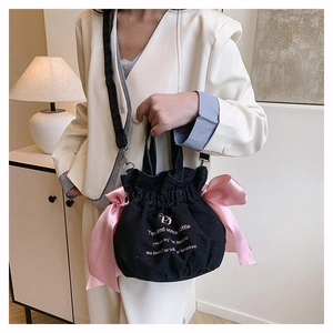 Détail du sac seau en denim noir avec des nœuds en satin rose et bandoulière