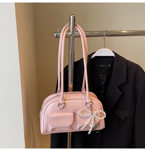 Detail of pink glossy shoulder bag with twin front pockets and pearl bow charm