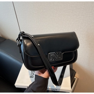 Close-up of black glossy PU leather handbag with silver metallic hollow logo buckle