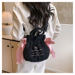 Détail du sac seau en jean noir avec de grands nœuds en satin rose et broderie rose