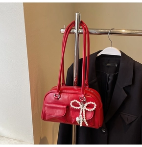 Detail of red leather shoulder bag featuring twin pockets and pearl bow heart charm