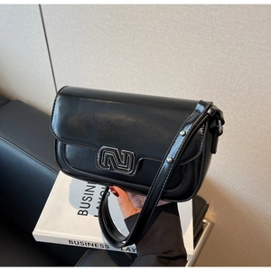 Detail of glossy black leather crossbody bag featuring a silver metal N logo on the flap