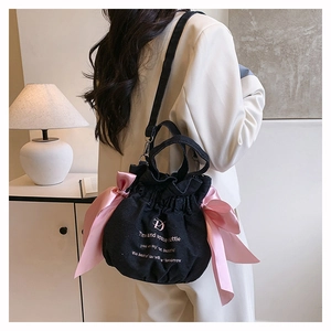 Détail du sac seau en denim noir avec nœuds en satin rose et lettrage logo artistique