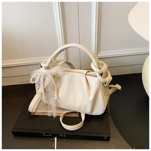 Detalle del bolso saco plisado crema con colgantes de perlas y un lazo de encaje