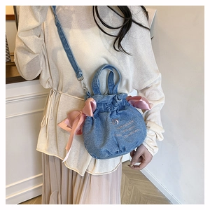 Détail d'un sac seau en denim avec nœud en satin rose et broderie sur un mannequin