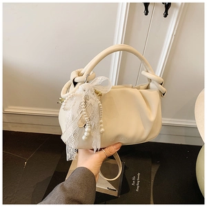 Detalle de bolso saco plisado beige con colgante de lazo de perlas y encaje fino