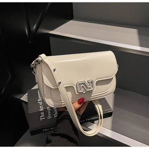 Close-up of cream faux leather square bag featuring a metallic logo and adjustable strap