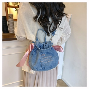 Détail du sac seau en jean bleu clair avec nœud en satin rose et broderie sur modèle