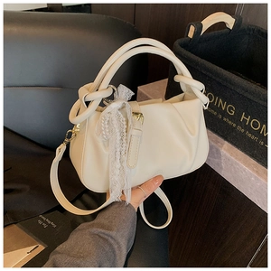 Detalle de bolso tipo cubo plisado beige con colgante de perlas de encaje y herrajes dorados