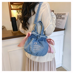 Détail du sac seau en denim bleu avec des nœuds en satin rose et des détails brodés
