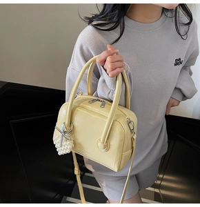 Detail of a creamy yellow leather Boston bag with pearl heart charm and golden logo