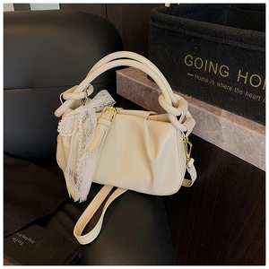 Detalle de bolso tipo cubo plisado crema con lazo de encaje y asa texturizada