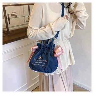Détail du sac seau en denim avec nœuds en satin rose et broderie sur la bandoulière