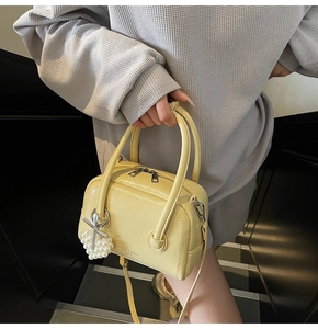 Detail of yellow leather Boston bag with pearl charm and silver zippers on a model