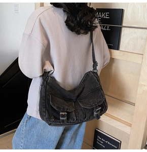 Detail of a large washed black denim messenger bag with vintage utility pockets and buckle