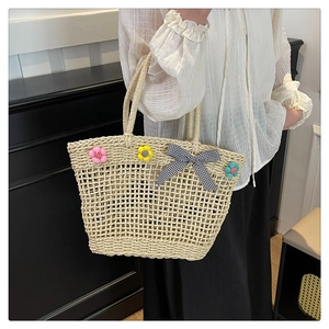 Detailed view of woven straw basket bag with 3D floral accents and checkered bow tie