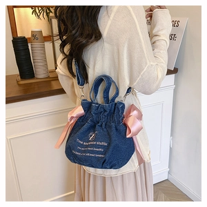 Détail du sac seau en jean bleu avec des nœuds en satin rose et un logo imprimé blanc
