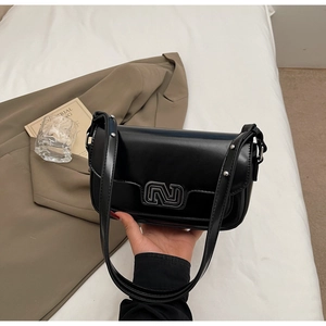 Detail of black glossy leather handbag featuring silver geometric logo and studded strap