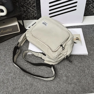Detail view of cream nylon crossbody bag with adjustable strap and front zipper pocket