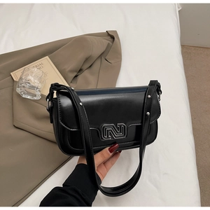 Close-up of black leather shoulder bag with silver geometric buckle and metallic studs