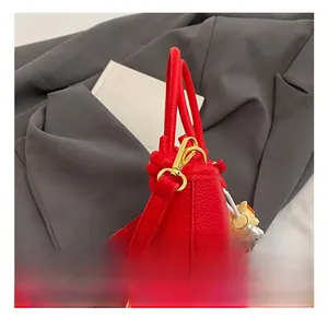 Detail of red lychee leather handbag featuring golden metal hooks and pearl charm