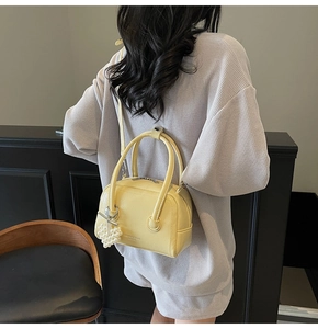Detail of yellow textured faux leather handbag featuring metal bow and pearl charm