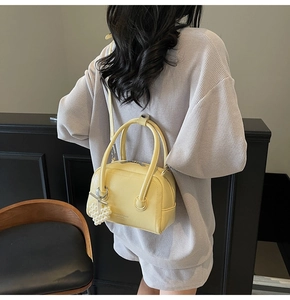 Detail of yellow pebbled leather Boston bag with pearl bow charm and shoulder strap