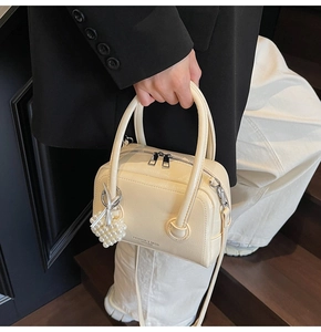 Detail of cream leather handbag with heart pearl charm and double zipper closure