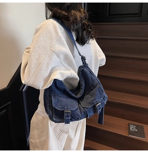Fashionable denim tote bag worn by model featuring dual front pockets with buckles