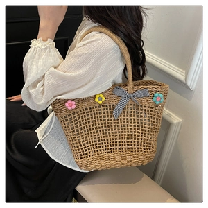 Detail of hand-woven straw basket bag featuring 3D floral accents and checkered bow